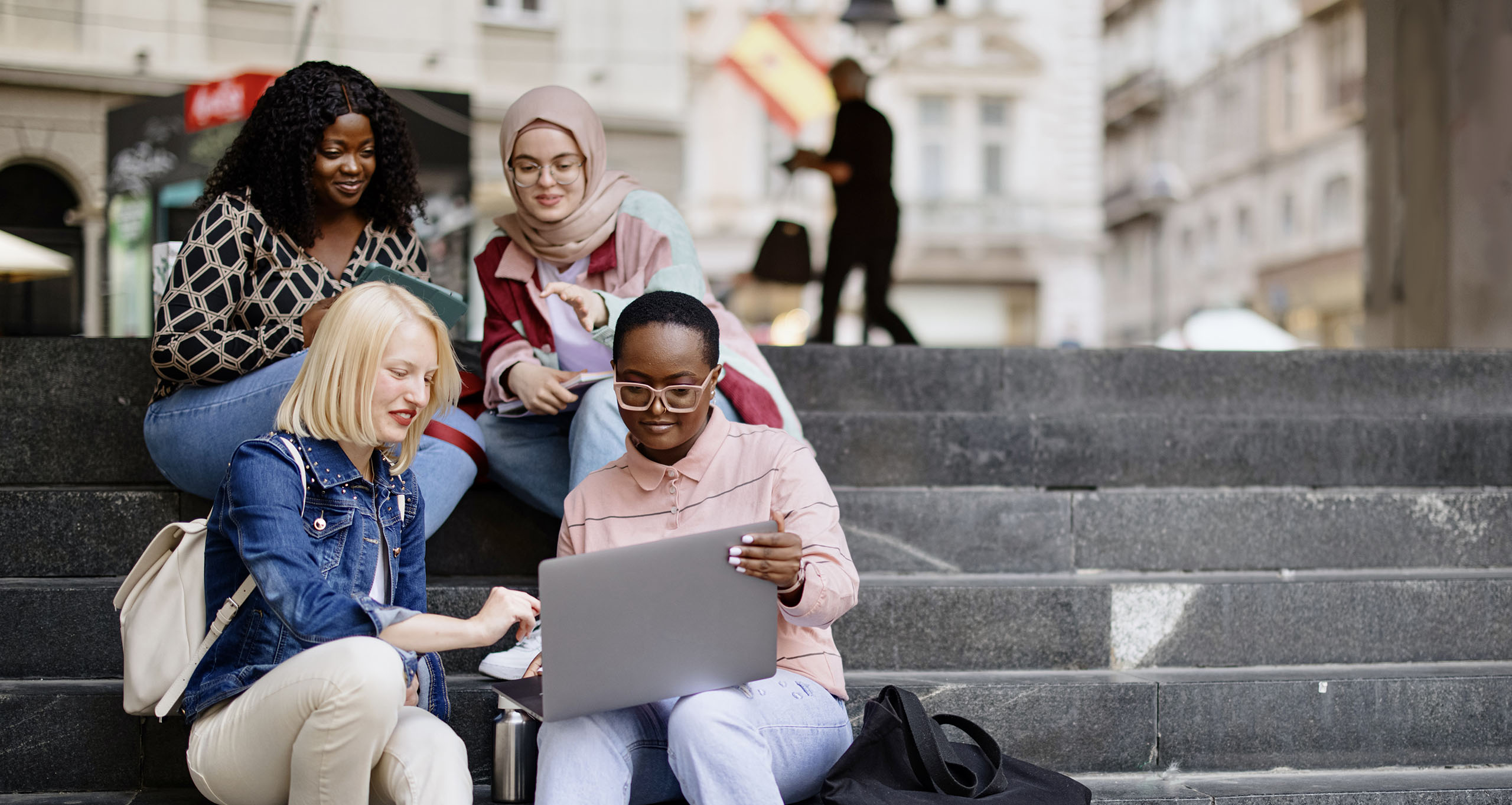 Students sit on the steps near the college and look at the laptop and digital tablet and talk